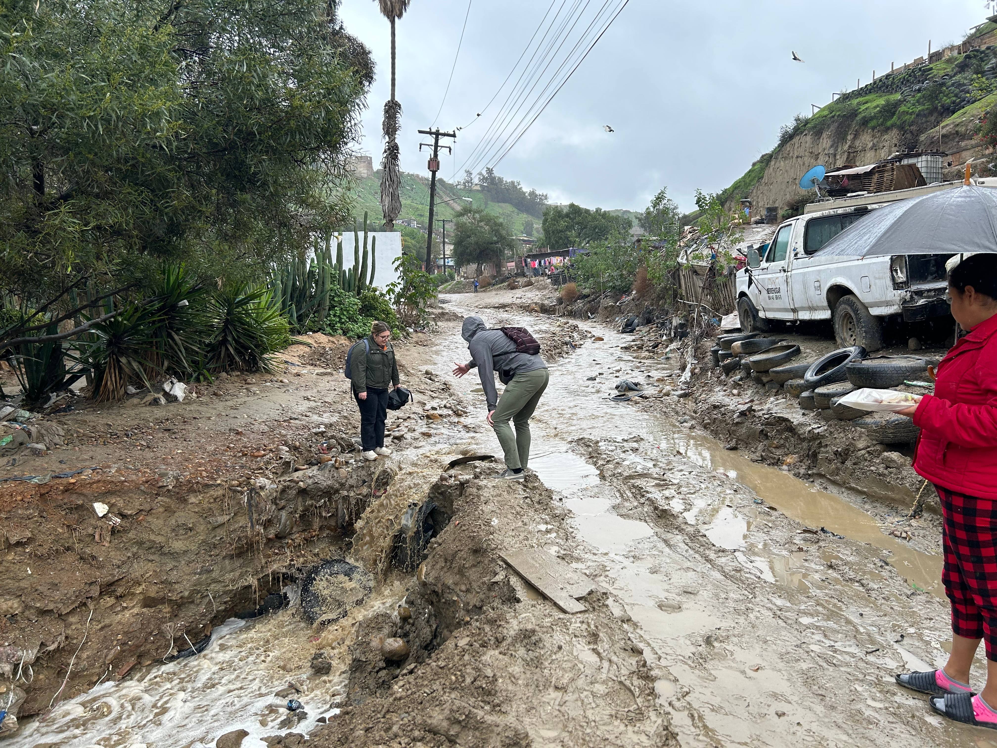 Community members navigating a flooded, eroded street after severe weather, showing the direct environmental impacts that drive displacement