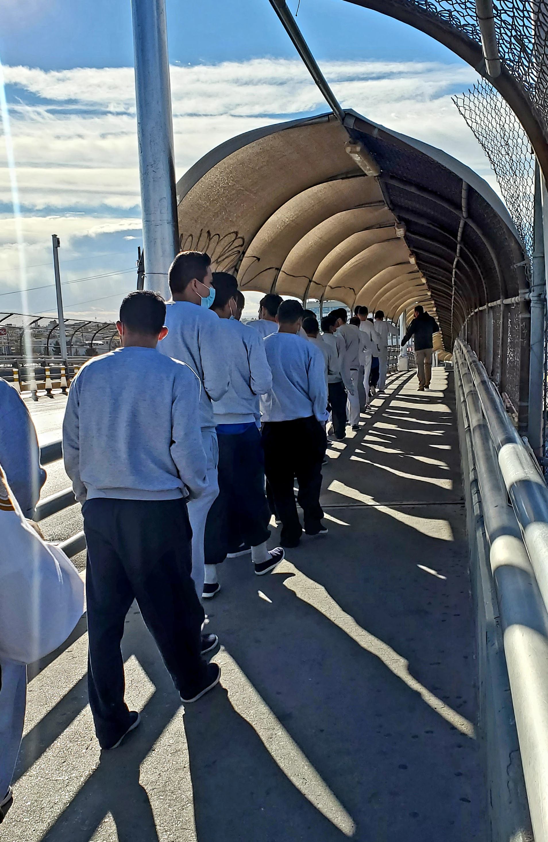 People walking in line at a U.S.-Mexico border crossing, depicting immigration enforcement operations