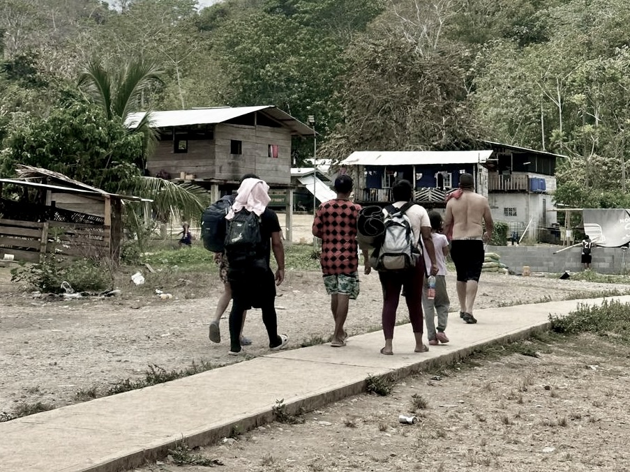 Migrants walking along a path through a village in the Darien Gap region, carrying backpacks on their journey through Central America